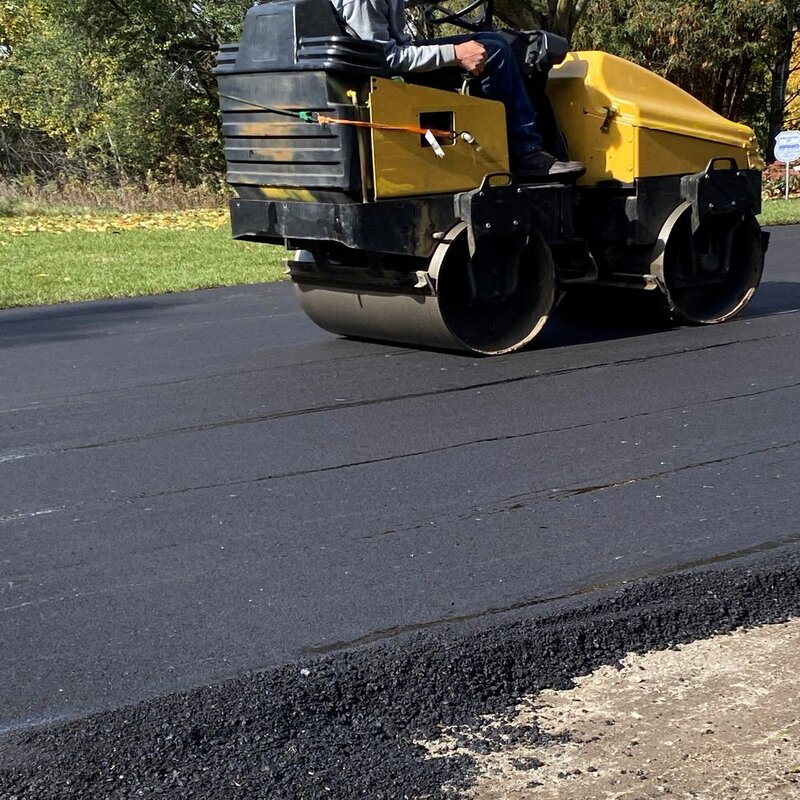 drive A yellow steamroller meticulously smoothing freshly laid asphalt, ensuring every inch is perfect for crack filling, all under the bright sun.