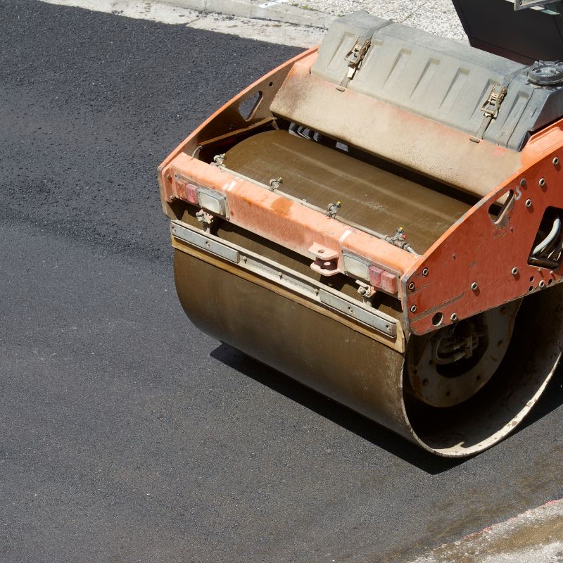Close-up of an orange road roller smoothing fresh asphalt, perfecting the parking lot paving on a busy street.