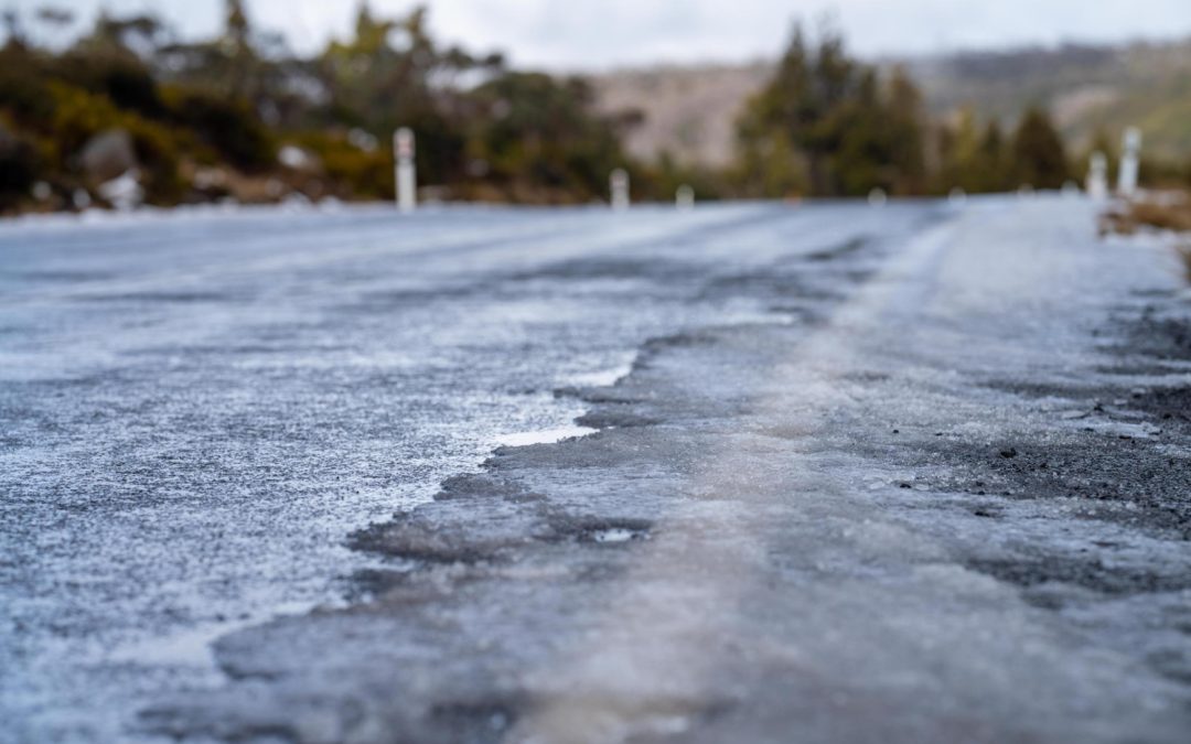A road covered in ice, with trees and hills in the blurry background on a cold day.